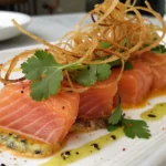 Close-up of a vibrant Salmon Crudo Recipe with crispy fried leeks, fresh cilantro, and thin serrano slices, showcasing sushi grade salmon under natural light.
