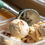 Homemade grape nut ice cream with creamy vanilla base and crunchy cereal bits being scooped from a freezer-safe container in natural light.