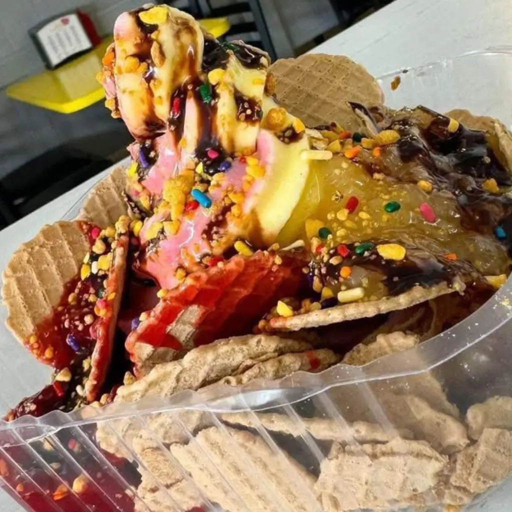 Colorful ice cream nachos made with waffle cone chips, swirled soft serve ice cream, fruit jelly, rainbow sprinkles, and chocolate syrup in a plastic tray
