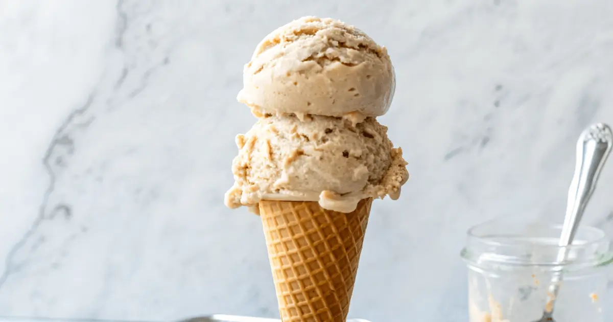 Two scoops of creamy Jamaican Grape Nut Ice Cream served in a waffle cone, showing visible cereal bits and a rich vanilla color.