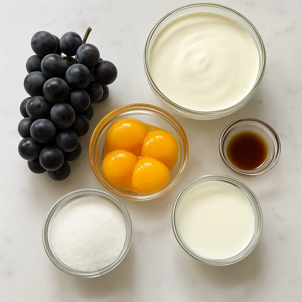 Close-up of ingredients for a grape ice cream recipe, including Concord grapes, cream, milk, sugar, and vanilla, arranged on a white kitchen surface.