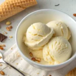 Bowl of homemade 2-ingredient ice cream with vanilla scoops, waffle cone, and chocolate pieces on a light background