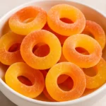 Bowl of homemade gummy peach rings coated with sugar, showing vibrant orange and yellow candy colors.
