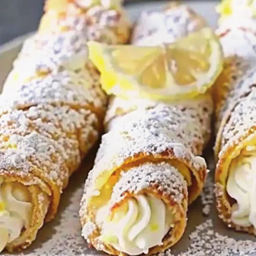 Close-up of three lemon meringue pie cannoli dusted with powdered sugar and topped with fresh lemon slices.