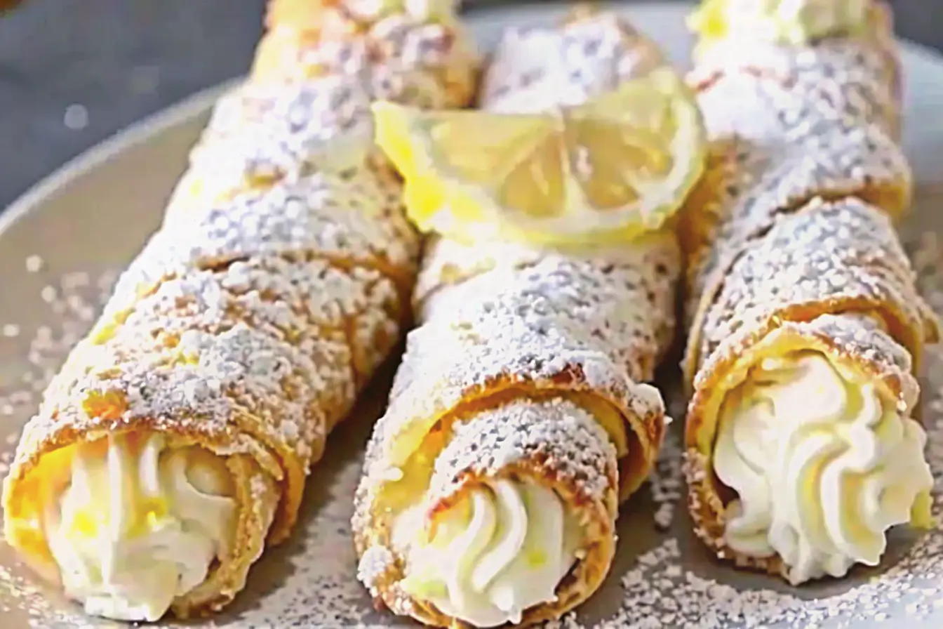 Close-up of three lemon meringue pie cannoli dusted with powdered sugar and topped with fresh lemon slices.