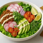 Raw vegan taco salad in a white bowl featuring walnut taco meat, sliced radishes, avocado, cherry tomatoes, red onion, fresh cilantro, and cashew dressing.