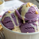Scoops of homemade Grapico ice cream with condensed milk drizzled on top, served in a paper cup on a rustic wooden table.