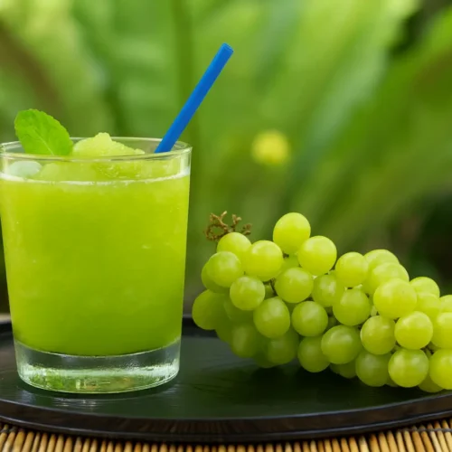 Refreshing glass of homemade green grape juice with ice, mint, and fresh grapes on a tray – healthy cold-pressed summer drink with lime