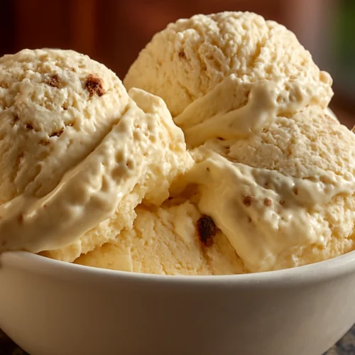 Creamy scoops of homemade Dr Pepper Ice Cream in a white bowl, with visible soda-infused texture and a spoon on the side