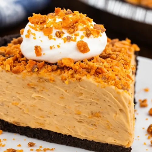 A slice of no-bake Butterfinger pie with peanut butter filling, chocolate crust, whipped topping, and crushed candy bar pieces.