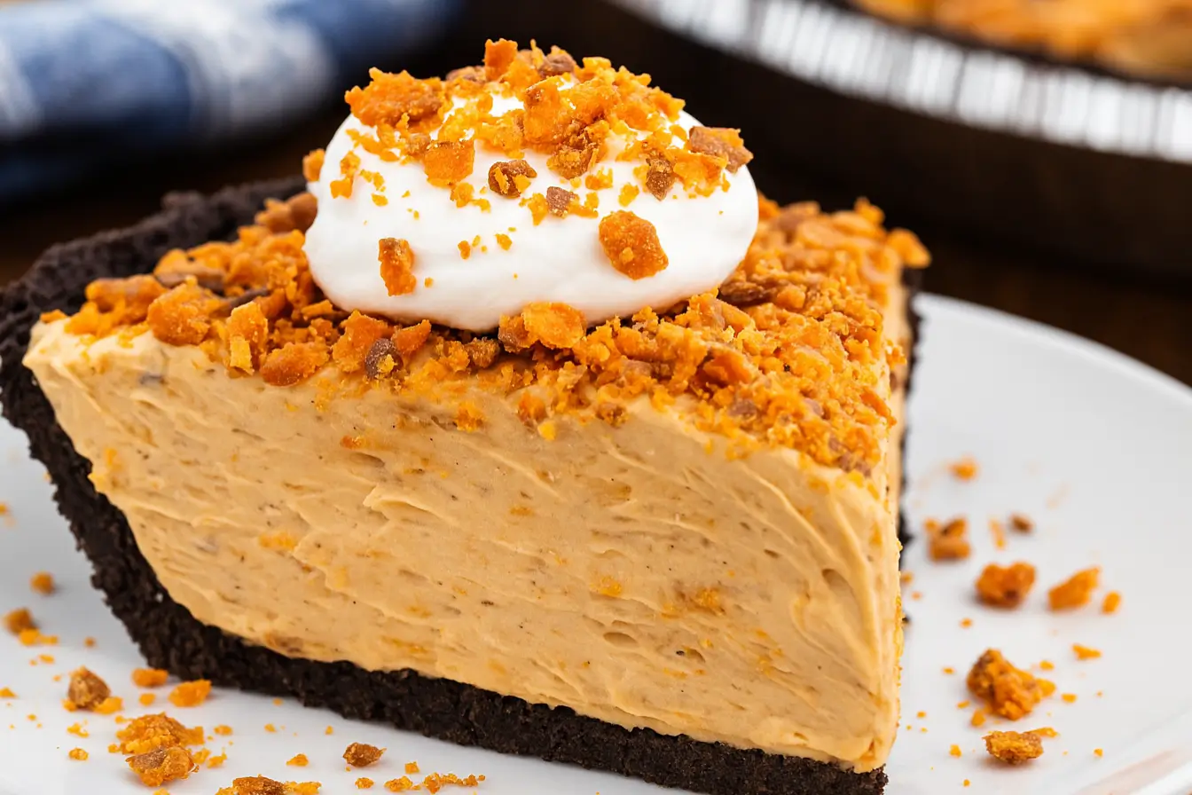 A slice of no-bake Butterfinger pie with peanut butter filling, chocolate crust, whipped topping, and crushed candy bar pieces.