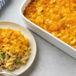 Freshly baked tuna casserole recipe with golden potato chip topping, noodles, peas, and creamy sauce in a white dish.