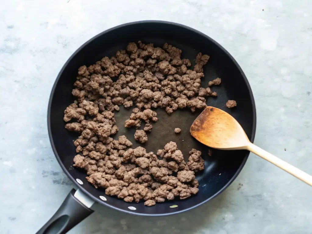Crumbled ground beef browning in a nonstick pan as the first step for cheeseburger quesadillas.