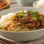 Egg roll in a bowl recipe with ground pork, cabbage, carrots, and rice topped with green onions and sesame seeds in a white bowl.