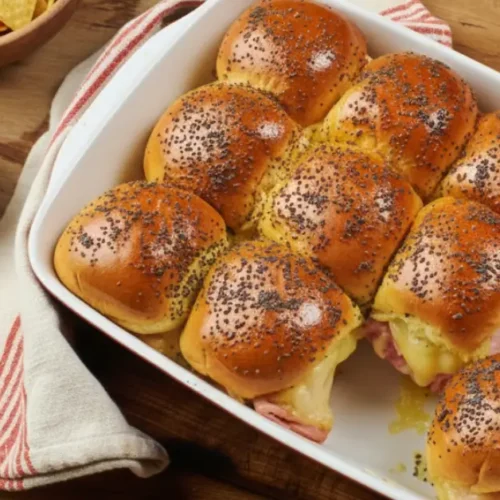 Golden-brown baked ham and cheese sliders on Hawaiian rolls, topped with a savory poppy seed butter glaze and melted Swiss cheese, served on a rustic wooden board.