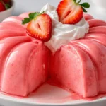 Pink gelatin recipe served in a glossy ring mold and topped with whipped cream, strawberries, and raspberries on a white plate