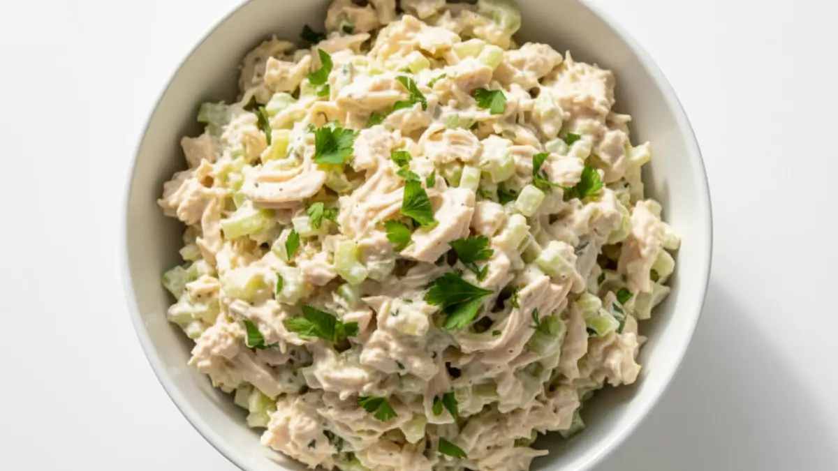 Healthy chicken salad recipe in a white bowl with shredded chicken, diced celery, parsley, and a creamy Greek yogurt dressing.