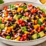 Colorful Cowboy Caviar Recipe served in a bowl with black beans, corn, avocado, fresh vegetables, cilantro, lime, and tortilla chips.