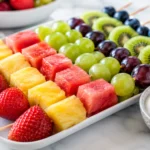 Colorful fruit kabobs on skewers served with a yogurt dip on a white platter