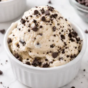 Creamy cottage cheese ice cream in a white ramekin topped with chocolate chips and crushed cookies for a high-protein no-machine dessert.