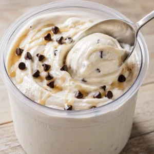 Ninja Creami cottage cheese ice cream in a pint container with mini chocolate chips, caramel drizzle, and a spoon scooping the creamy texture.