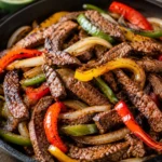 Sizzling flank steak fajitas with charred peppers and onions in a cast-iron skillet